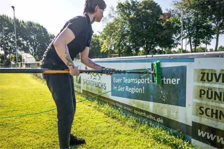 Reinigungskraft reingt Werbebanden mit einem Reinigungsgeraet.