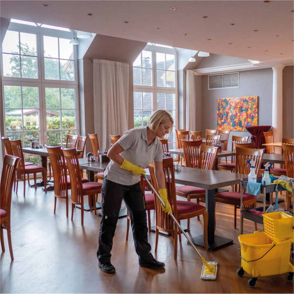 Reinigungskraft reinigt Fussboden im Hotelsaal.