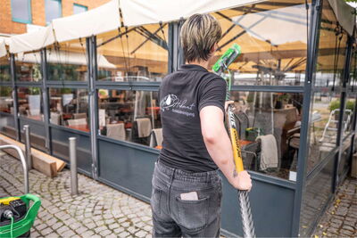 Reinigungskraft reinigt Glasfront mit einem Reinigungsgeraet.