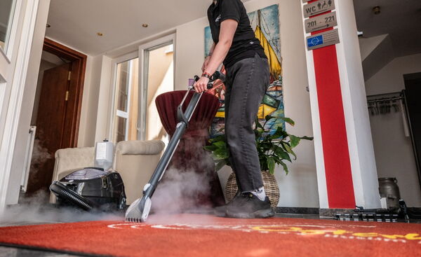 Reinigungskraft reinigt mit Dampfreiniger den Teppichboden