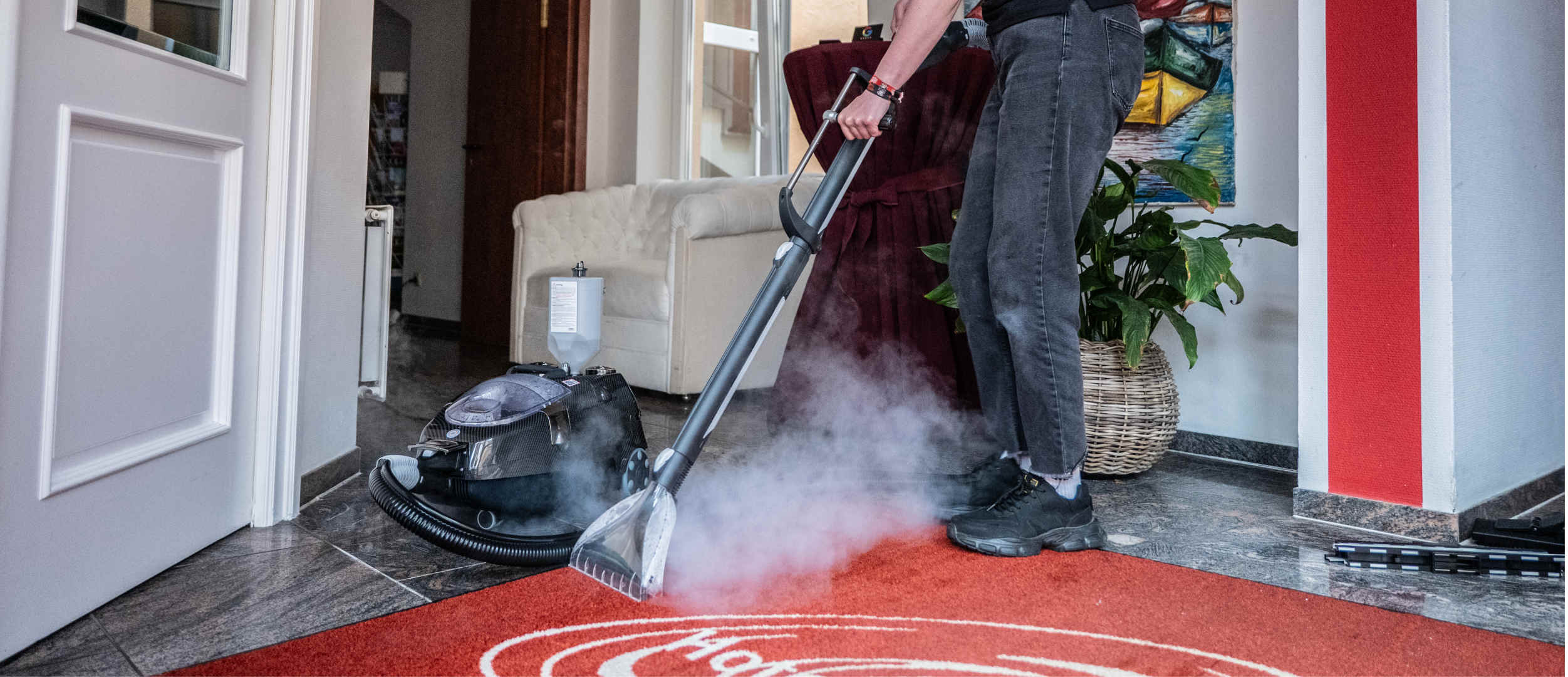Reinigungskraft reinigt Teppichboden mit Dampfreiniger im Hotel.