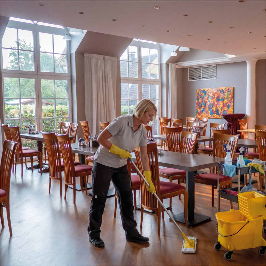 Grundreinigung in Geschaeftsgebaeude. Eine Frau reinigt den Fussboden mit einem Wischer.