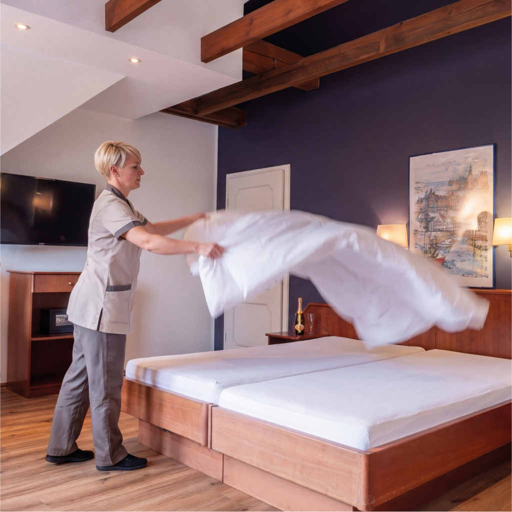 Unterhaltsreinigung in Ferienunterkuenften und Geschaeftsraeumen. Reinigskraft richtet die Bettbezuege im Hotelzimmer.
